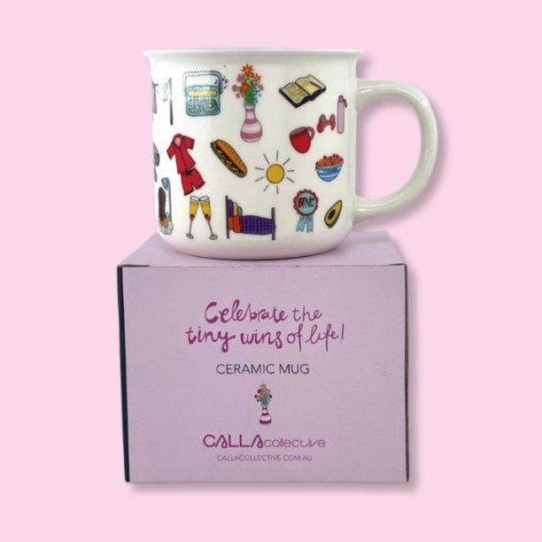 A white ceramic mug with colorful illustrated icons, displayed on top of its lavender gift box against a solid pink background. The box features the brand name 'CALLacollective' and the text 'Celebrate the tiny wins of life! CERAMIC MUG'.