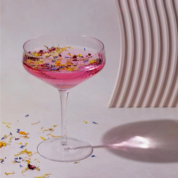 Pink cocktail in a glass with floral toppings on a light background