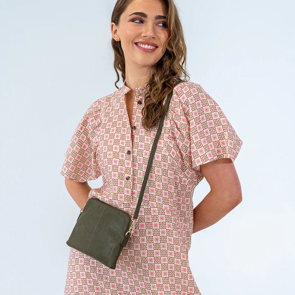 Woman wearing a patterned dress with a green crossbody bag against a light blue background