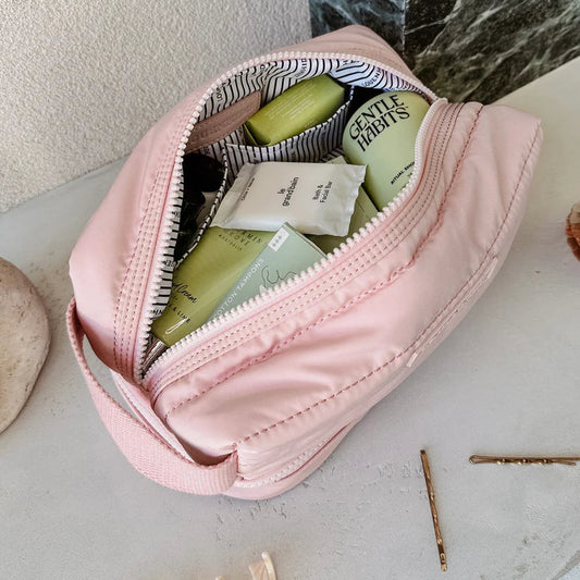 Pink cosmetic bag with green bottles and striped fabric on a light surface.