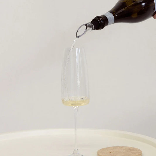 Wine bottle pouring white wine into a clear glass on a light background