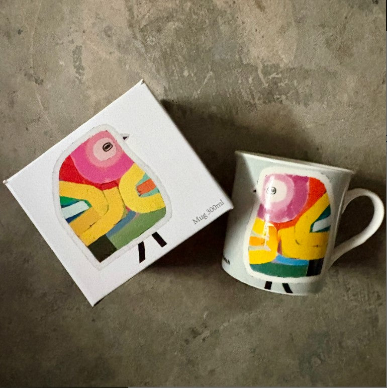 Colorful mug with bird design next to its packaging on a concrete surface