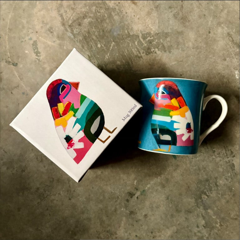 Colorful mug with abstract design next to its packaging on a textured surface
