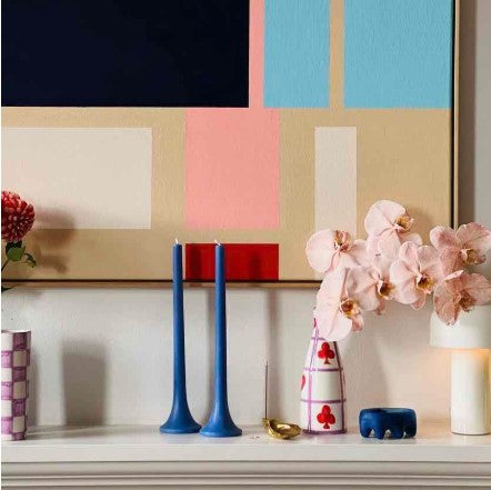 Decorative shelf with blue candles, a floral arrangement, and colorful abstract art in the background.