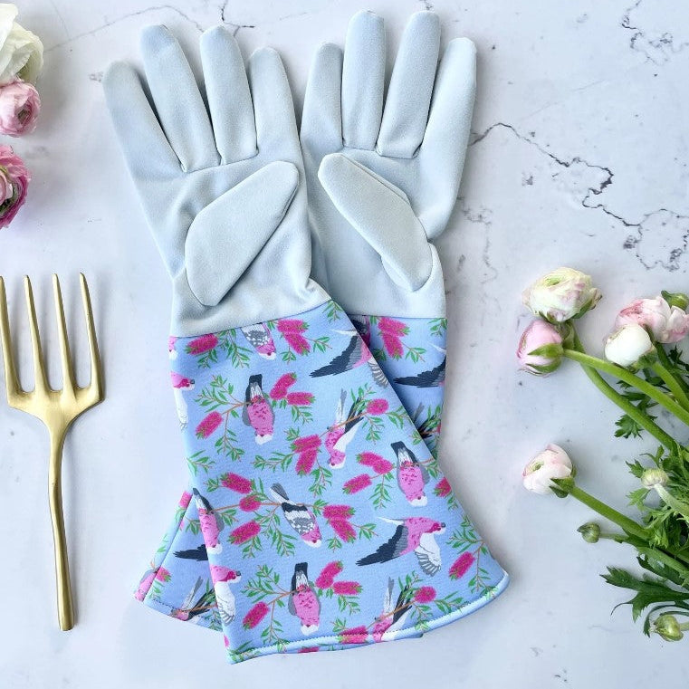 Gardening gloves with floral pattern on a marble surface with flowers and a fork.