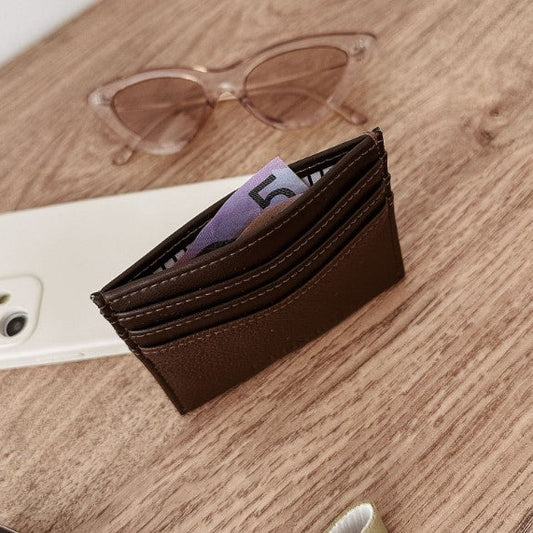 Brown wallet with money on a wooden surface next to a phone and sunglasses