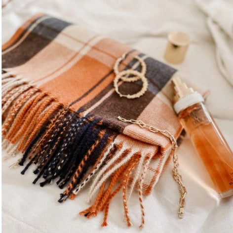 Plaid scarf with fringe, necklace, and bottle on a light background
