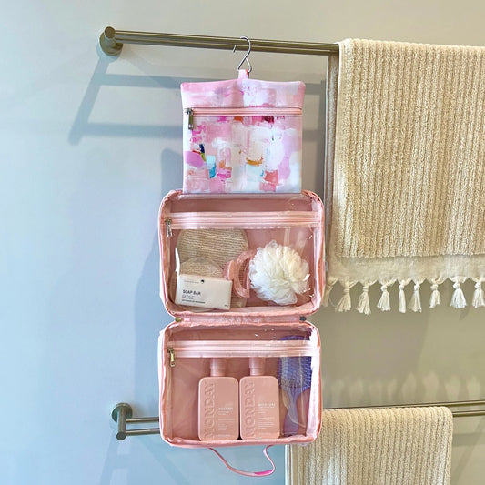Pink hanging toiletry bag with travel items on a towel rack