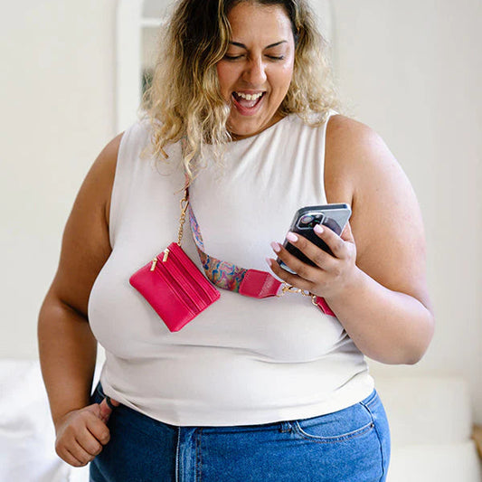 Woman in a white sleeveless top and blue jeans holding a phone and pink wallet.