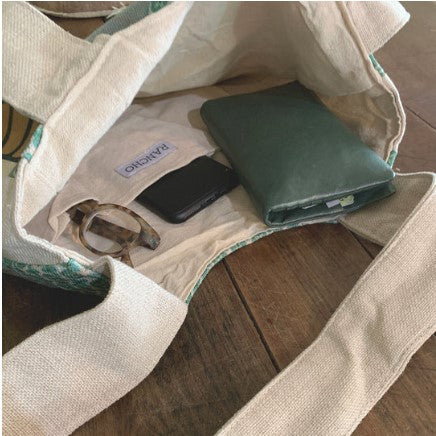 Open beige tote bag with a green wallet and phone on a wooden surface