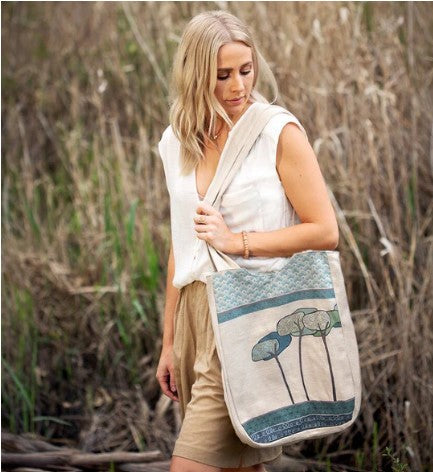 Woman holding a tote bag with a nature-themed design in a natural setting