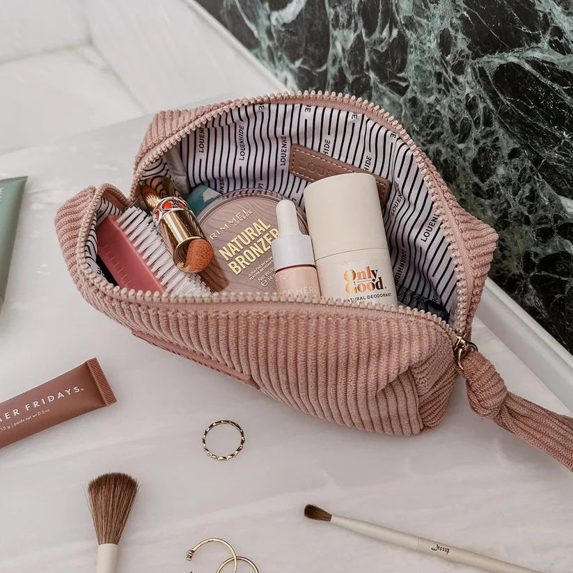 Pink corduroy makeup bag with cosmetic products on a marble surface