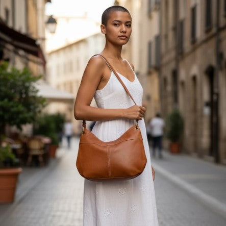 Woman in a white dress holding a brown leather handbag on a city street.