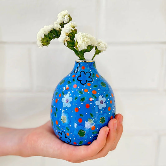 Hand holding a blue vase with floral patterns and white flowers against a white background