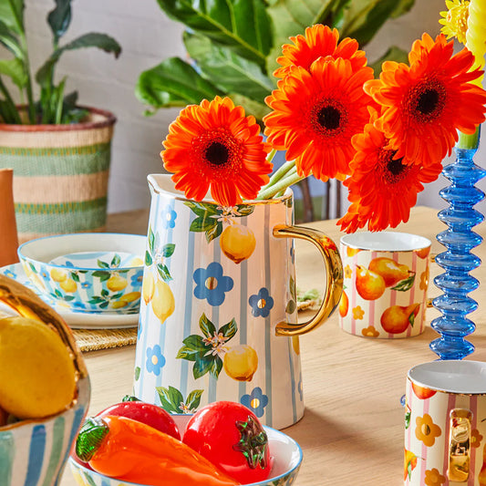 Colorful table setting with a pitcher, bowls, and mugs on a wooden surface.