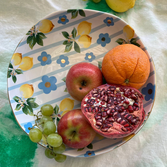 Fruit including apples, oranges, and a pomegranate on a decorative plate with lemon and flower patterns.