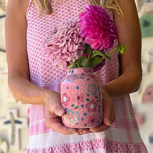 Person holding a pink floral-patterned jar with flowers, wearing a matching dress.