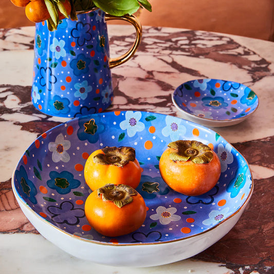 Decorative ceramic bowl with persimmons and a matching vase on a marble surface.