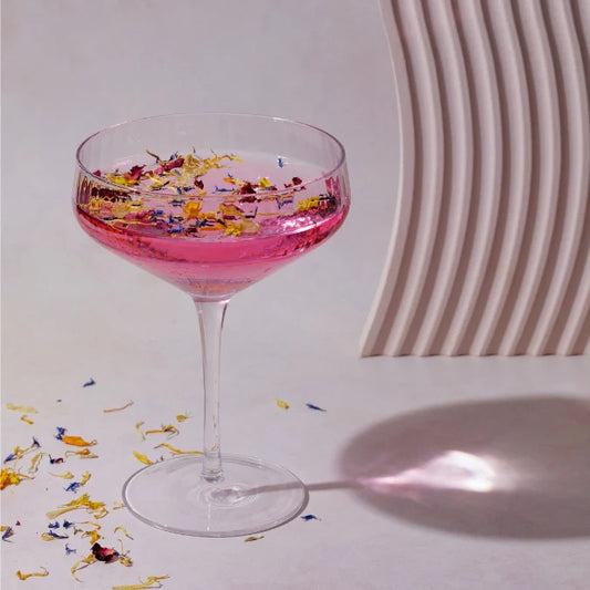 Pink cocktail in a glass with floral toppings on a light background