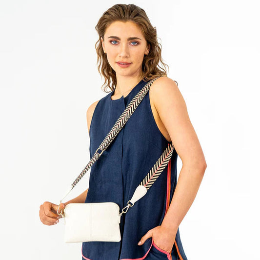 Woman wearing a navy sleeveless top and pants with a white crossbody bag on a white background