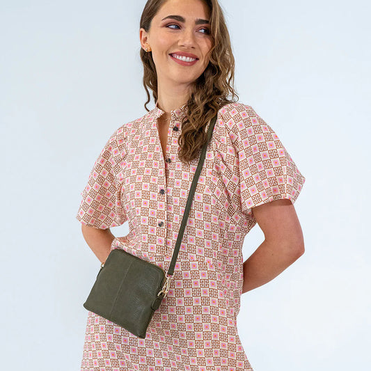 Woman wearing a patterned dress with a green crossbody bag against a light blue background