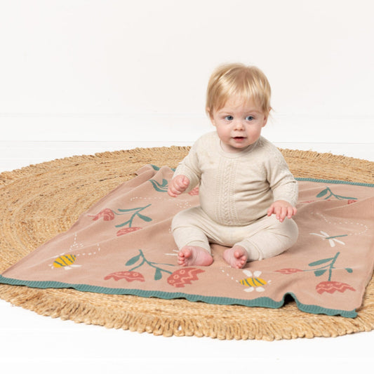 Baby sitting on a floral blanket with a wicker basket in the background