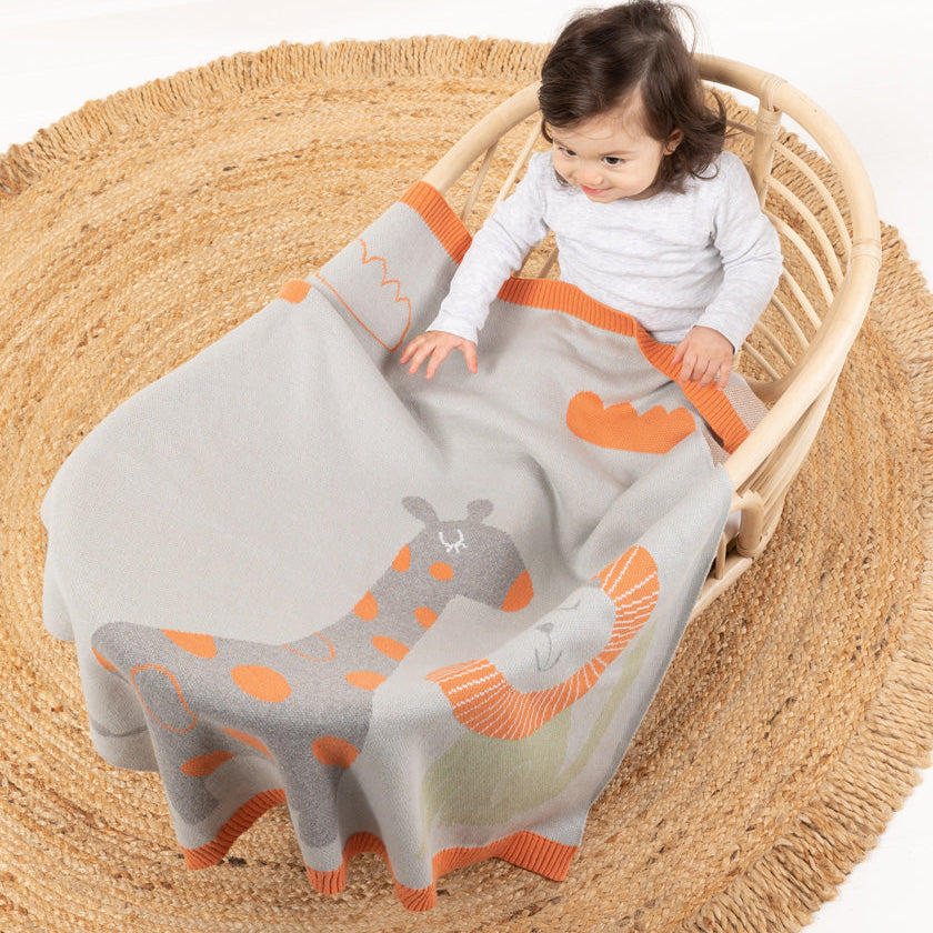 Child in a crib with a giraffe-themed blanket on a white background