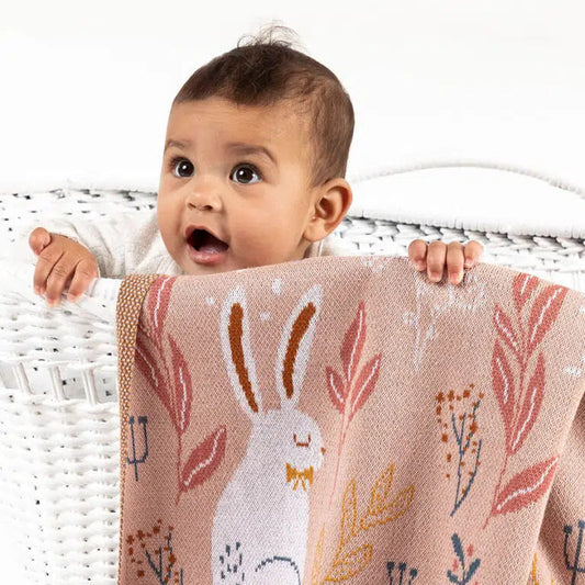 Baby holding a pink blanket with bunny and floral patterns