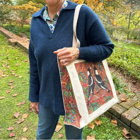 Person holding a tote bag with bird design in an outdoor setting