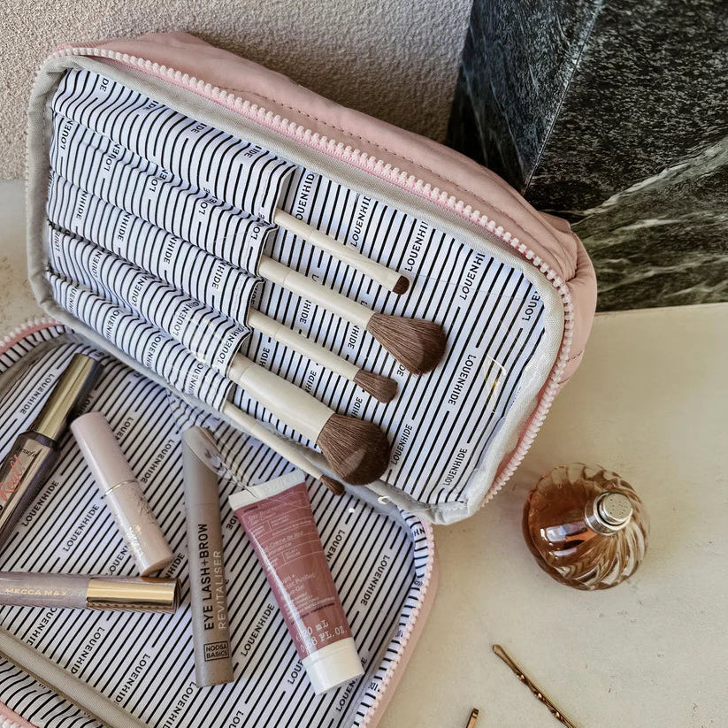 Makeup brushes and products in a striped makeup bag on a marble surface