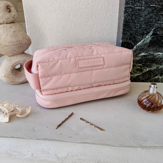 Pink cosmetic bag with 'LOUENHIDE' branding on a light surface with a bottle and hairpins.