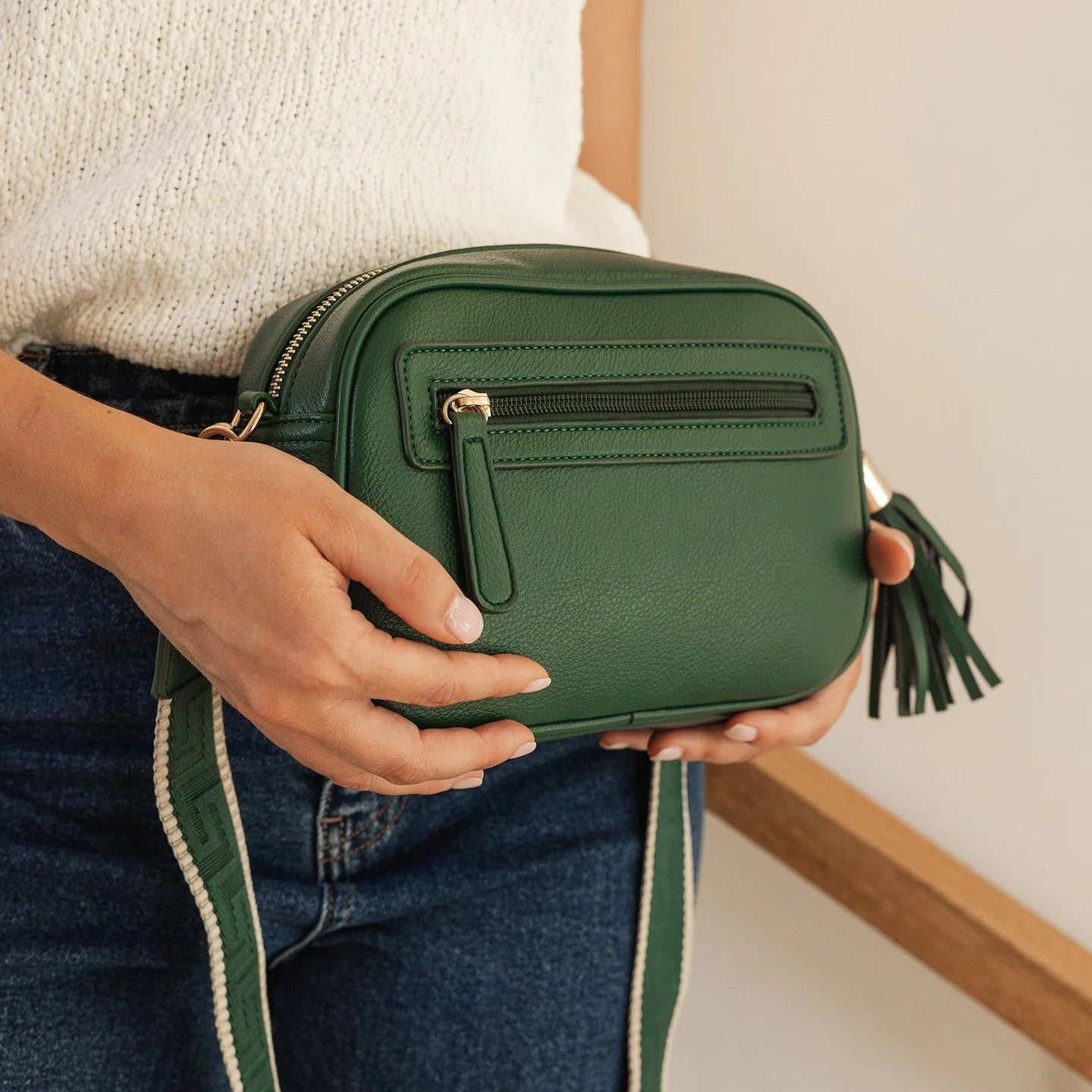 Green crossbody bag held by a person with a neutral background