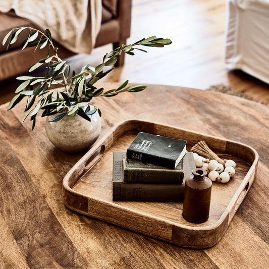 Wooden tray with books, a bottle, and decorative items on a wooden table.