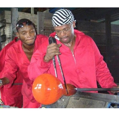 Two people in red jackets working with glassblowing tools and molten glass.