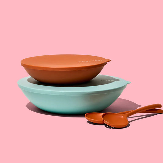 Two bowls, one teal and one brown, with a spoon on a pink background