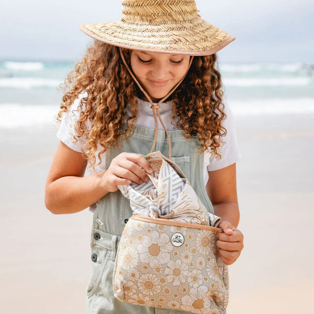 Young girl holding a floral-patterned bag & beach towel on a beach