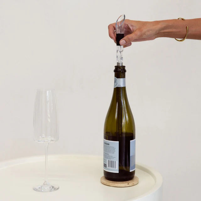 Person using a wine bottle stopper to open a bottle of wine on a white surface.