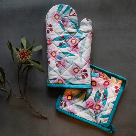 Floral oven mitt and pot holder set on a dark surface with a plant.