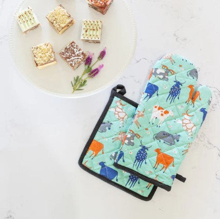Set of colorful animal-patterned pot holders on a light surface with a plate of food in the background.