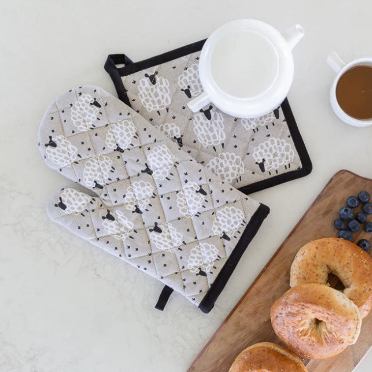Oven mitt and pot holder with black and white pattern on a kitchen counter with bagels and coffee.