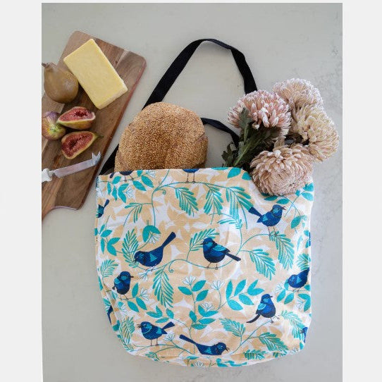 Reusable shopping bag with bird and leaf pattern on a surface with items like figs and cheese.