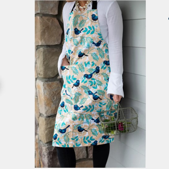Person wearing a floral apron with blue birds and green leaves, standing against a stone wall.