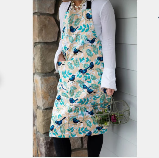 Person wearing a floral apron with blue birds and green leaves, standing against a stone wall.