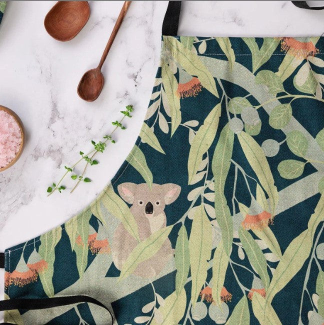 Floral apron with a koala design on a marble surface with wooden spoons and a bowl.