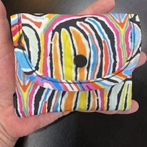Colorful striped pouch held in a hand against a dark background
