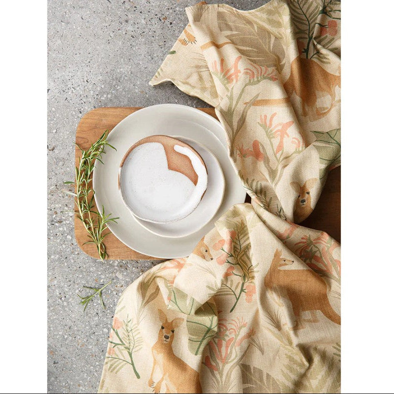 Dinner setting with white plates, a wooden cutting board, and a floral cloth on a textured surface.