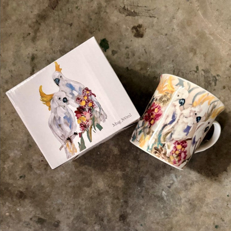 Decorative mug with bird design next to its packaging on a concrete surface