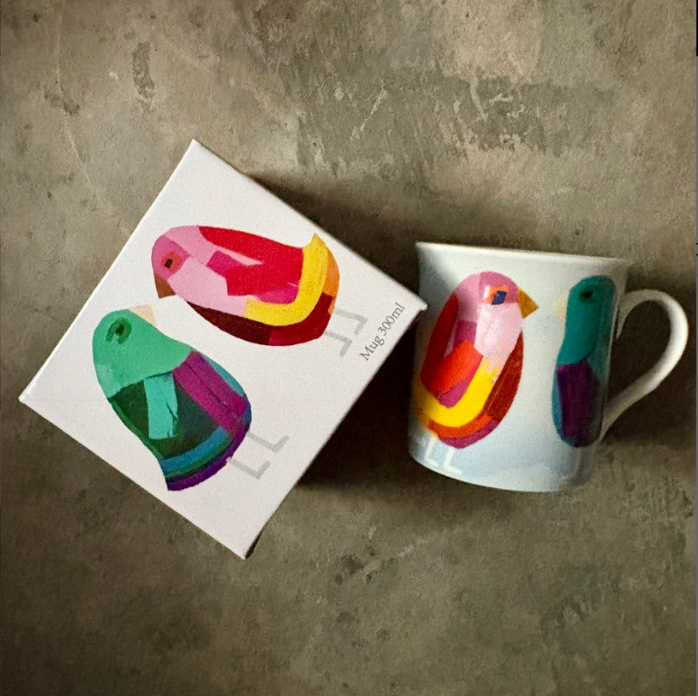 Colorful mug with bird design next to its packaging on a concrete surface