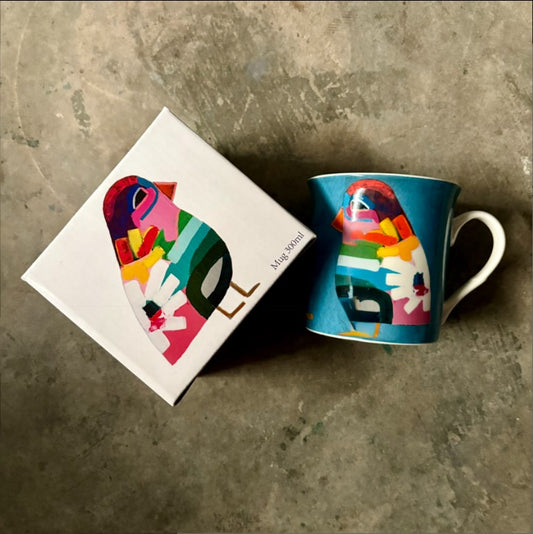 Colorful mug with abstract design next to its packaging on a textured surface