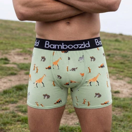 A man wearing Bamboozd boxer briefs with a light green background and an animal print, standing outdoors with his arms crossed.